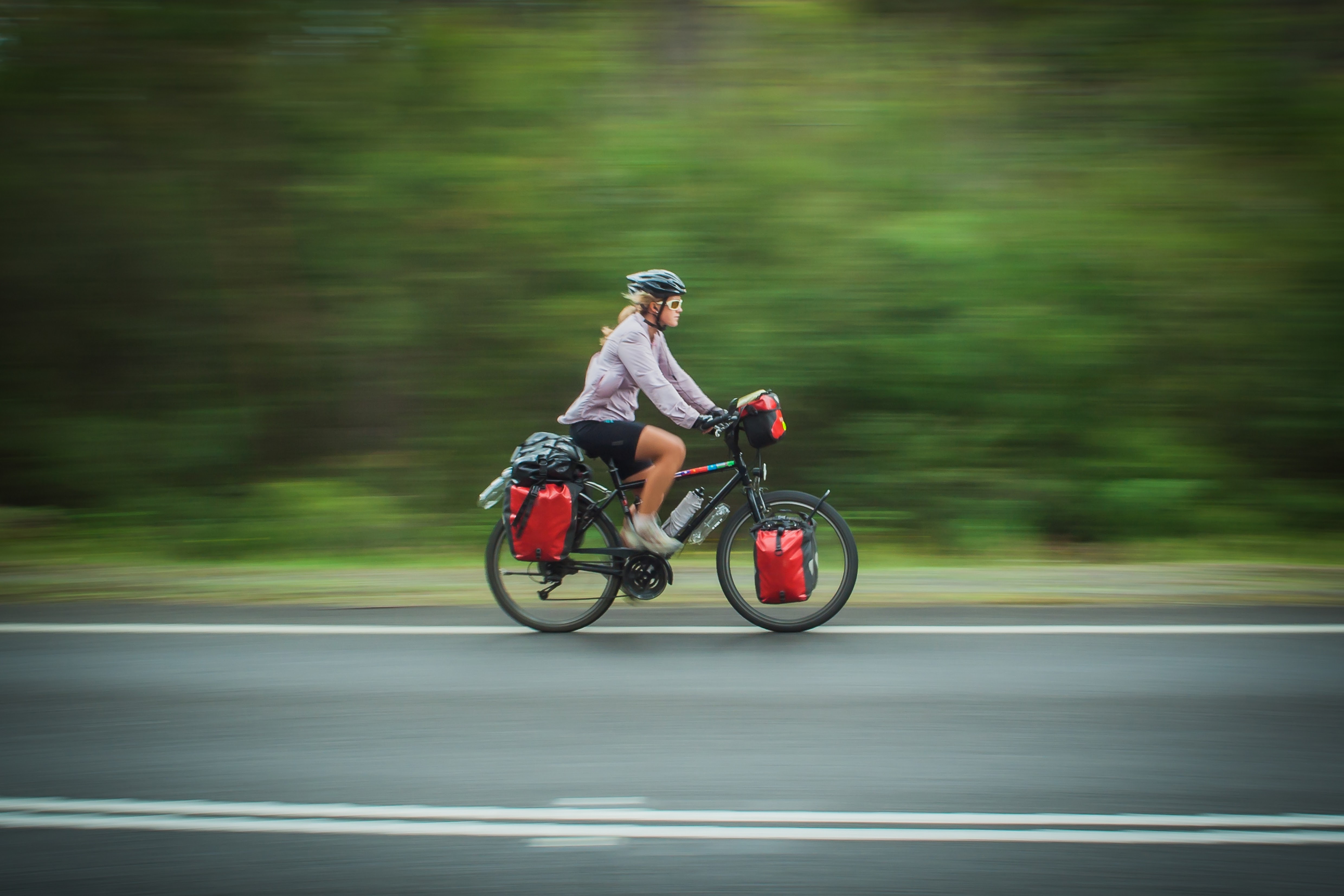 A person rides a bike on a paved road in the center of the frame, facing to the right of the frame.