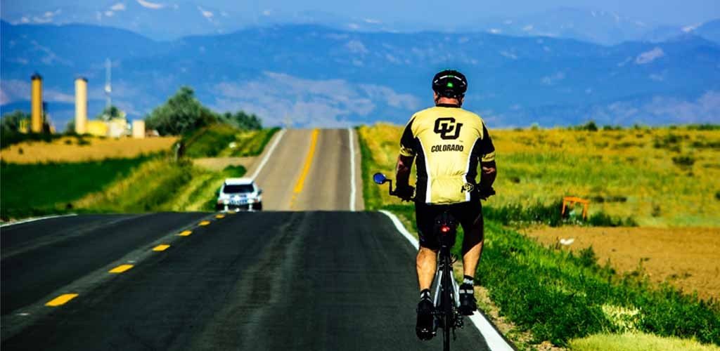 man in Colorado jersey as he rides outside of Greeley with a clear and big view of the rocky mountains