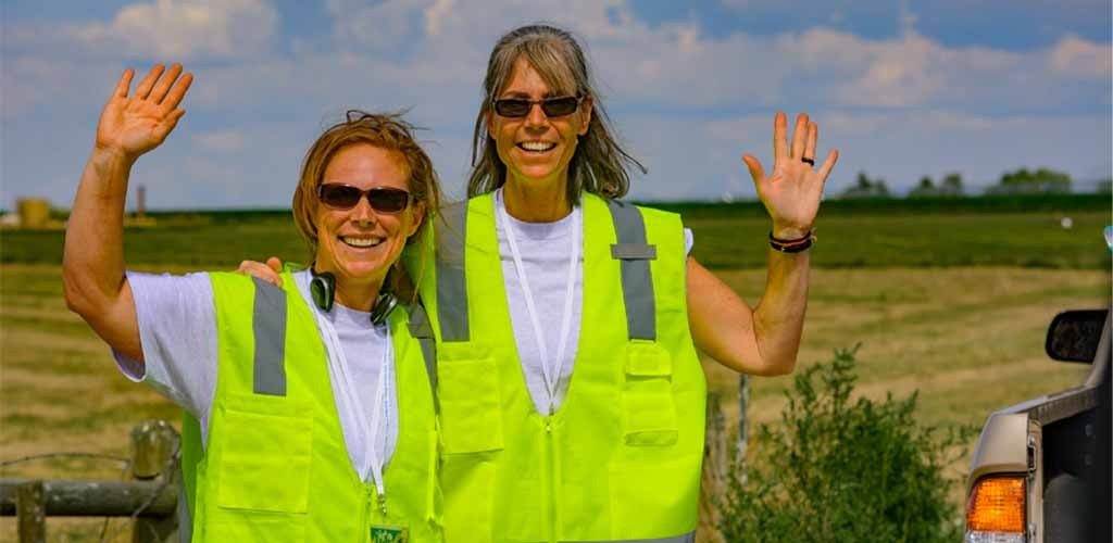 Two people in yellow safety vests waving at the camera