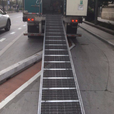 A delivery truck parked blocking a bike lane with their loading ramp.