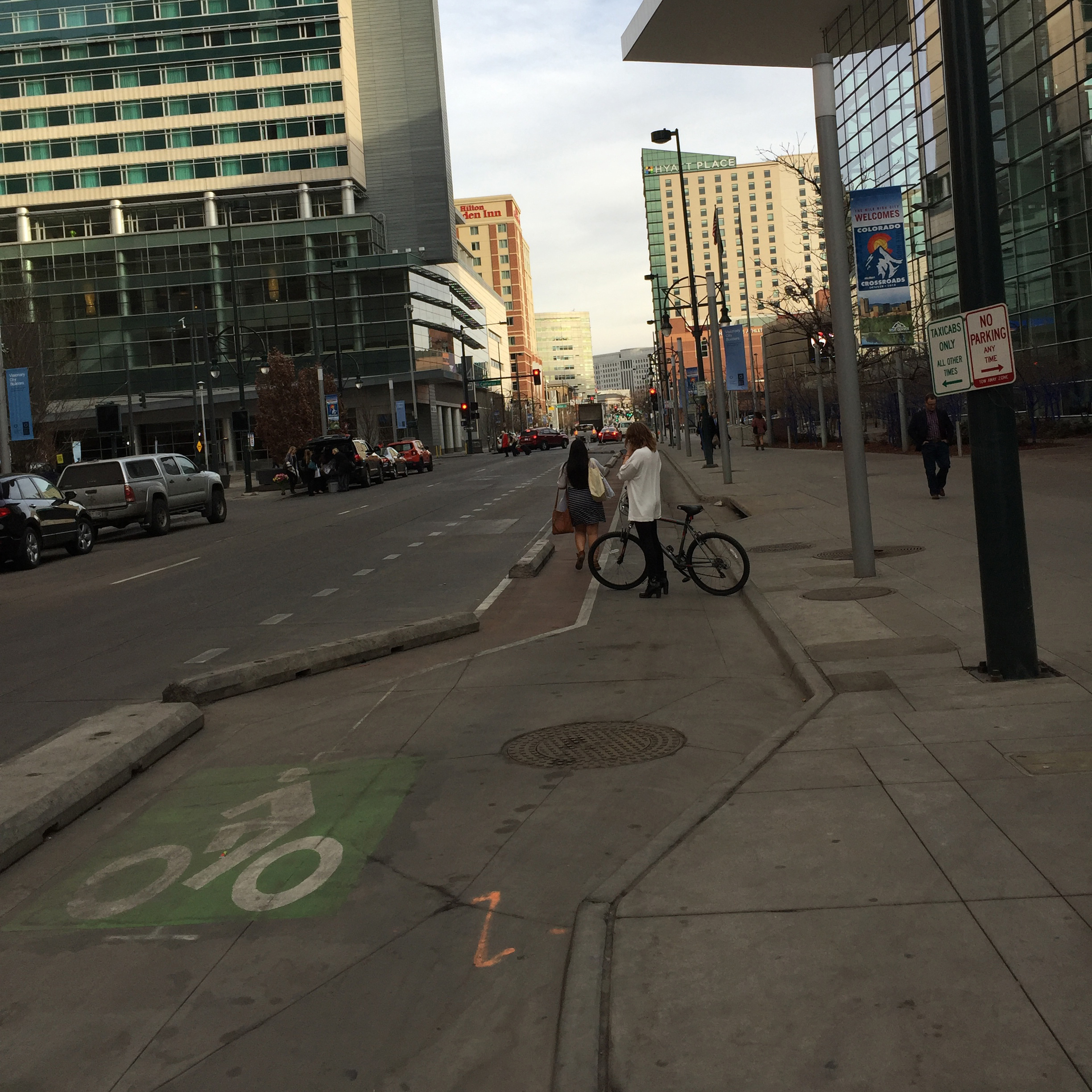 A person standing with their bike across a bike lane in downtown Denver.
