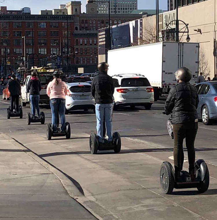 Five people riding segways in the bike lane in a city.