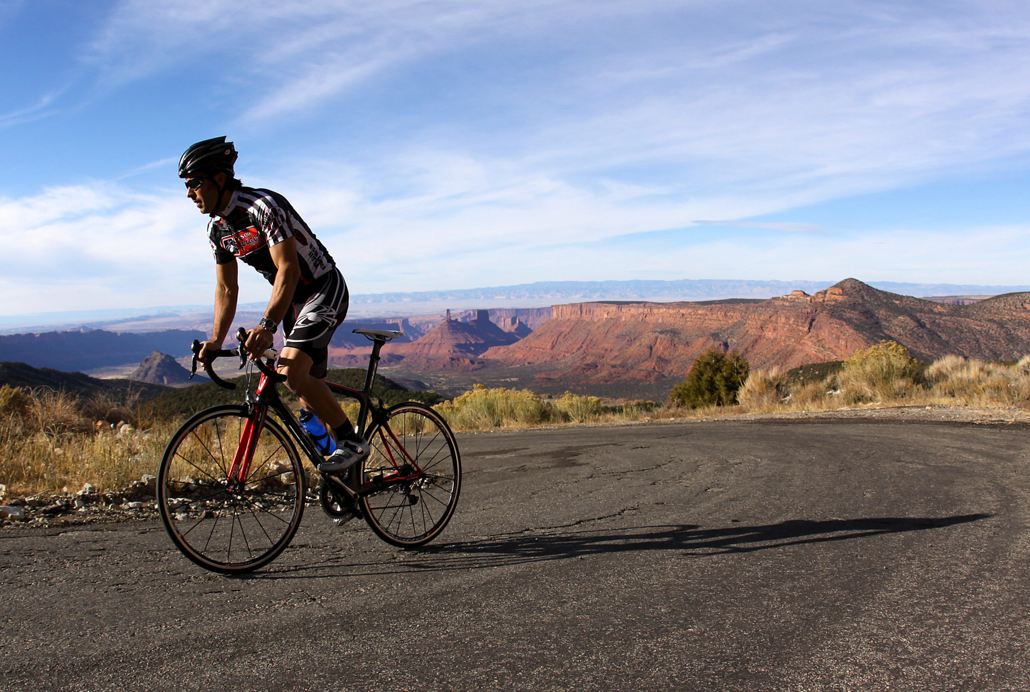 A person riding a bike up a curve in a paved road high above red rock formations.