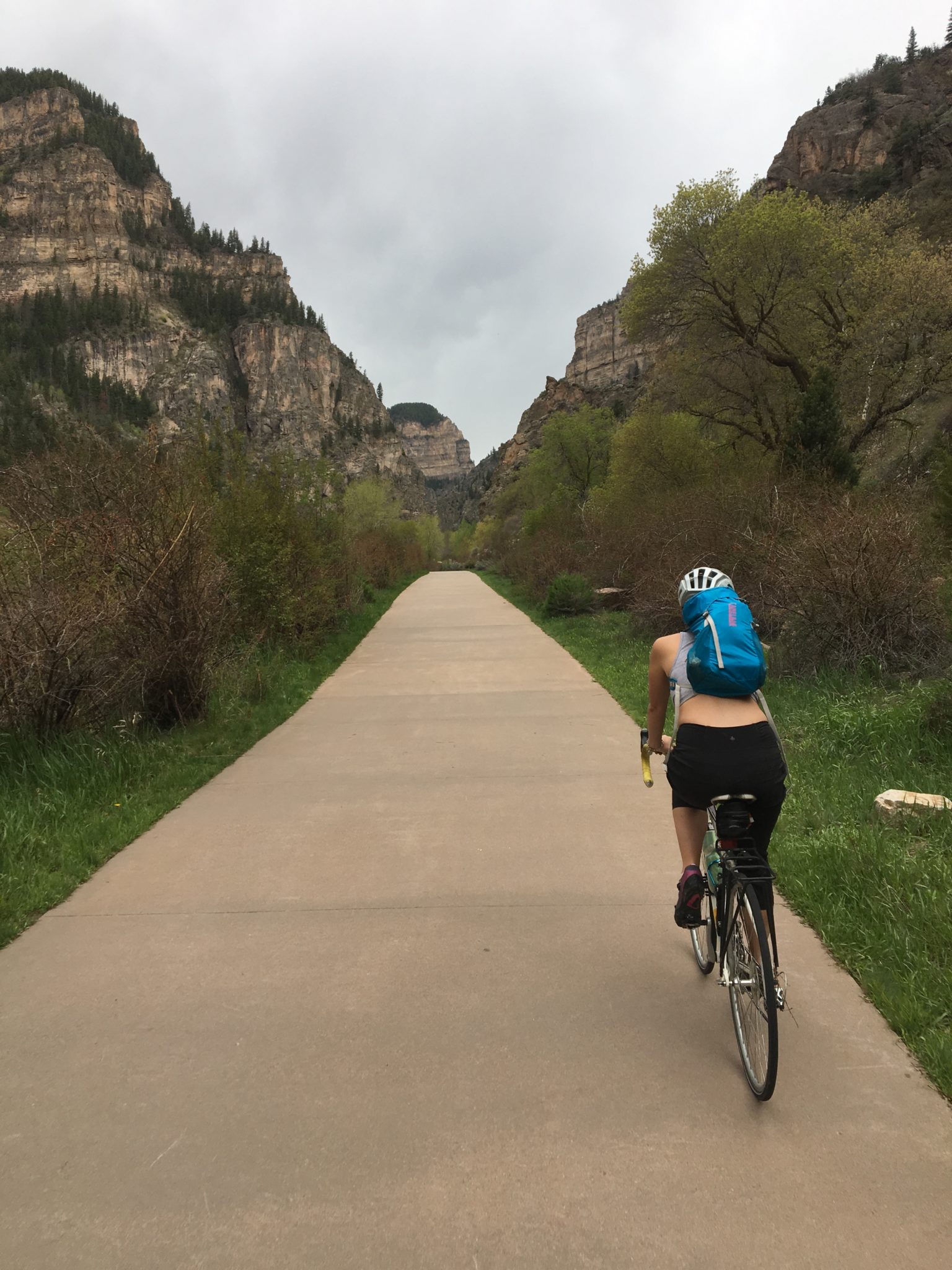 A person riding a bike on a paved trail between tall cliffs.