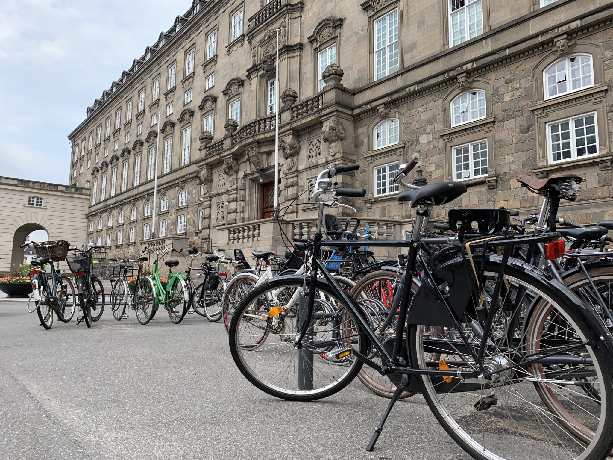 Many bikes parked to bike racks in front of a building in Copenhagen.