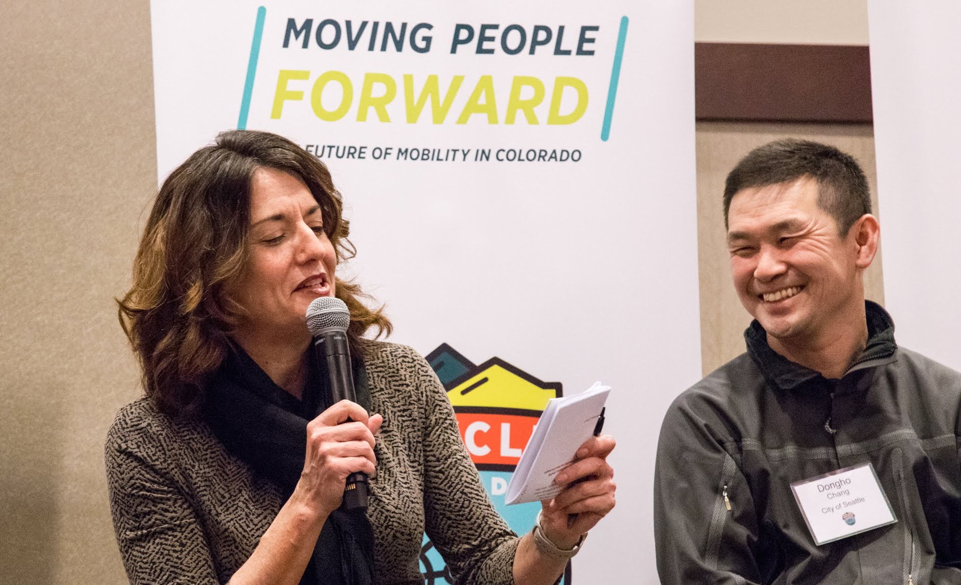 Two people speaking at Moving People Forward. One person is speaking into a handheld mic.