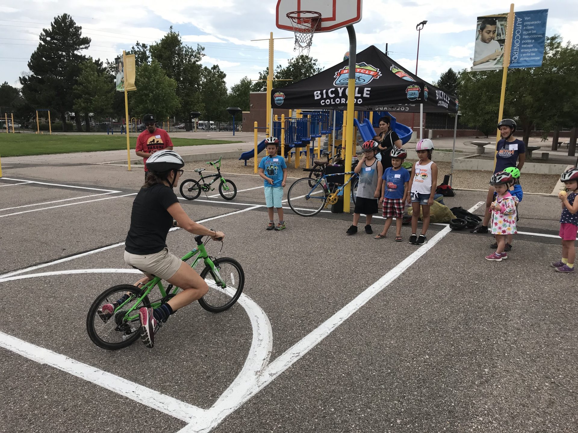 An adult demonstrating gliding on a bike to a group of children in a playground.