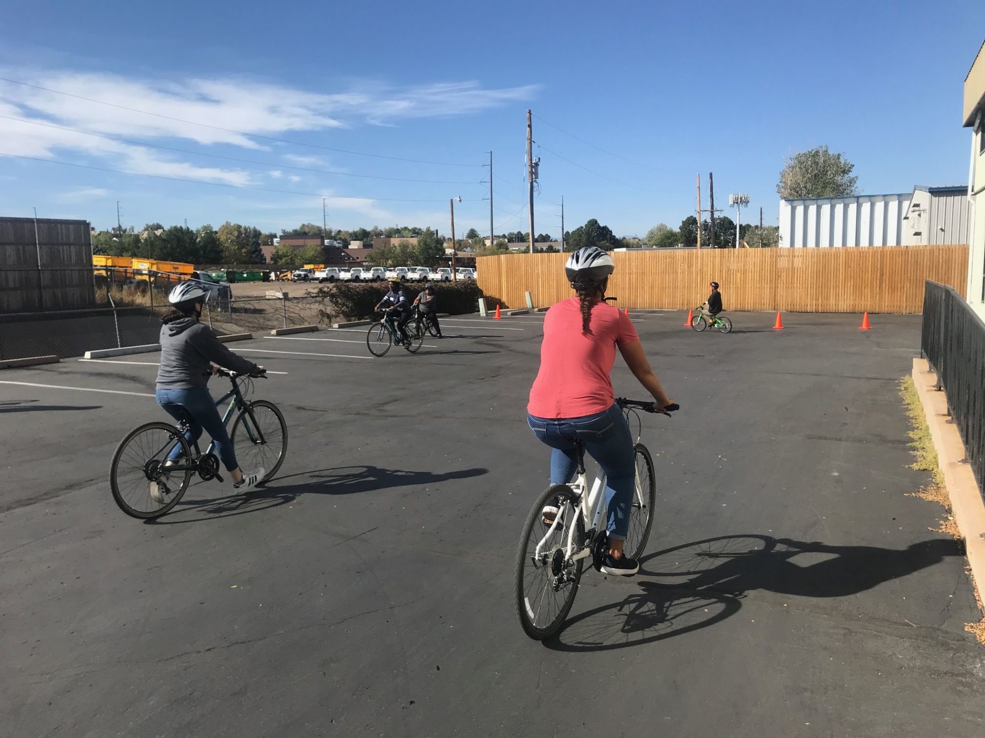 Adults and children learning to ride bicycles in a parking lot.