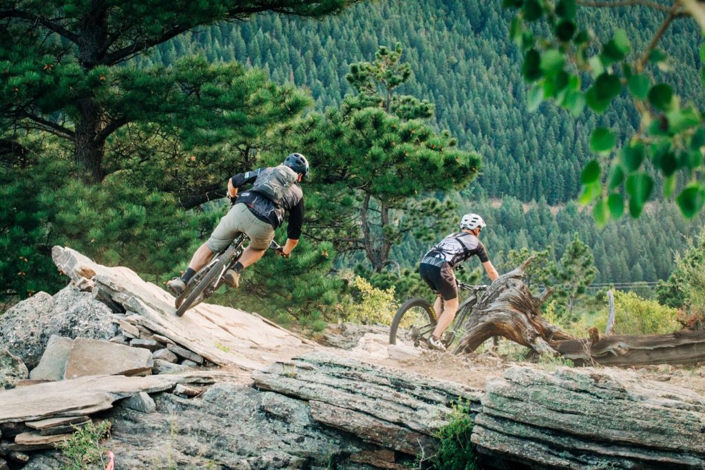 Two people riding mountain bikes on a trail with rocks away from the camera.