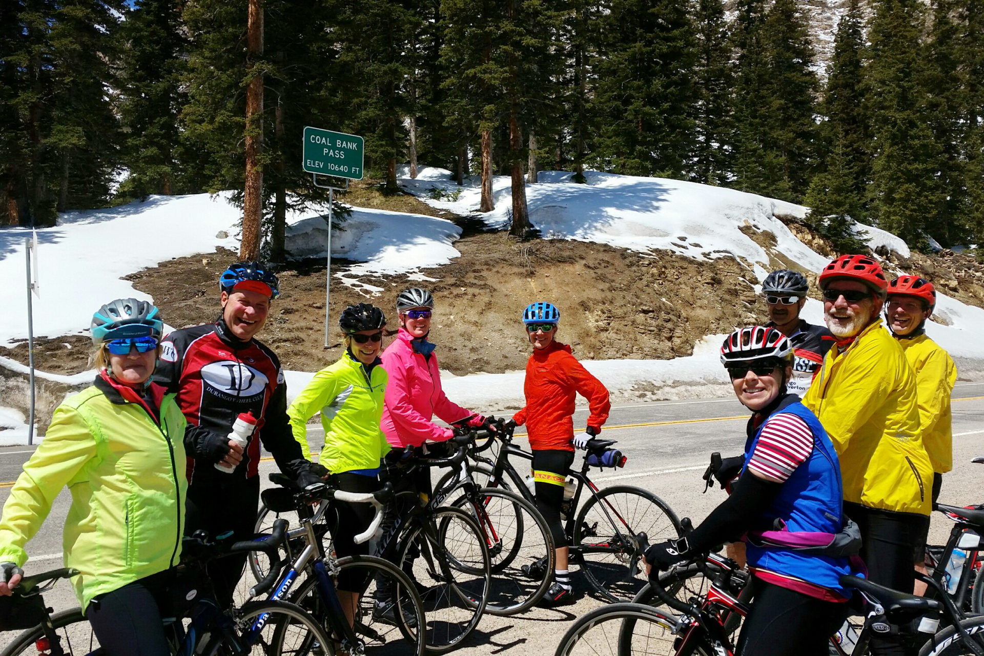 Nine people stand with their bikes on a mountain road.