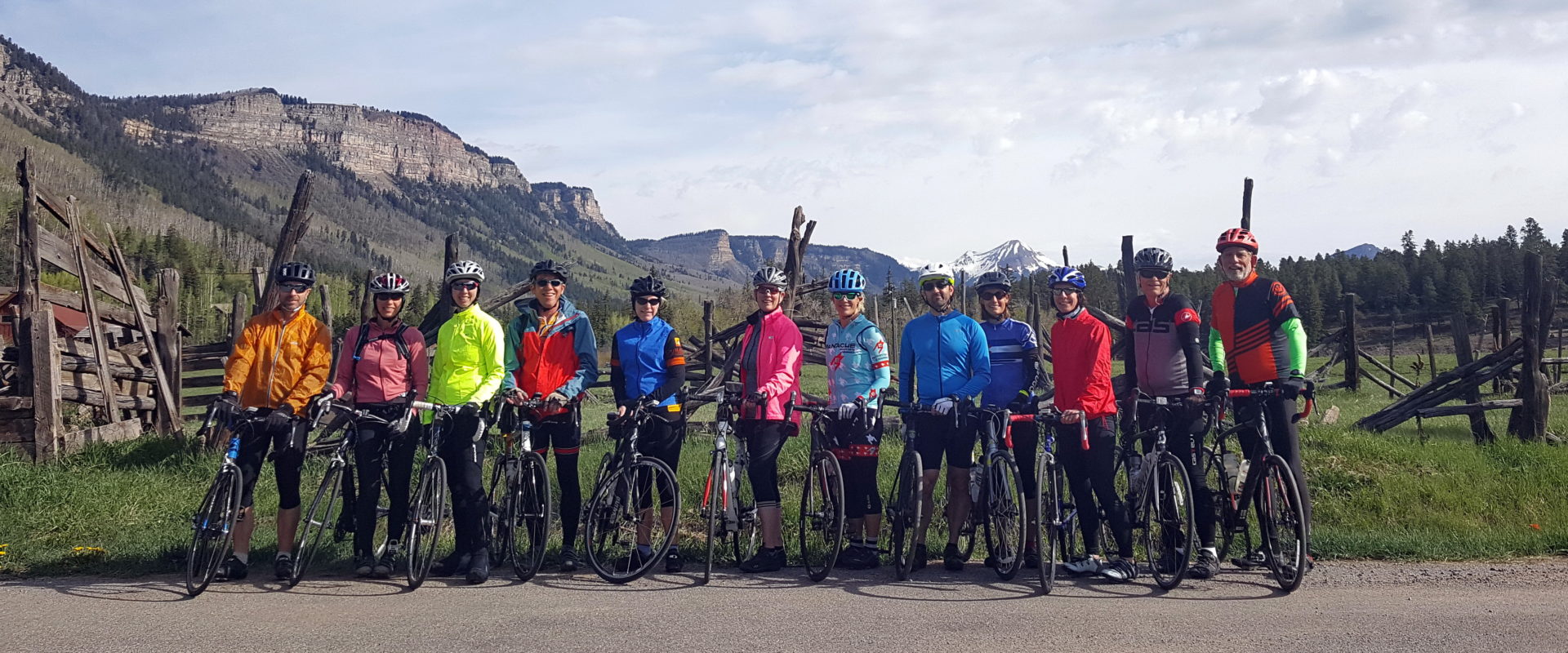 Twelve people standing with their bikes on the side of a road. There are mountains in the background.