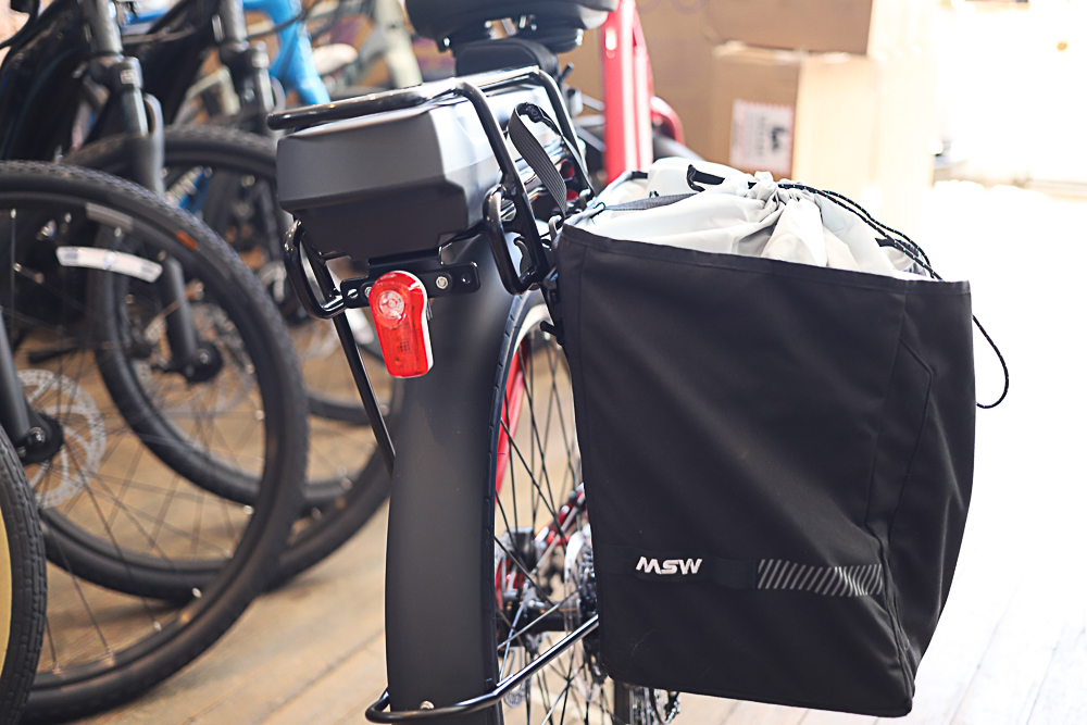 The rear of a bike with a red rear light, a rack and a pannier bag.