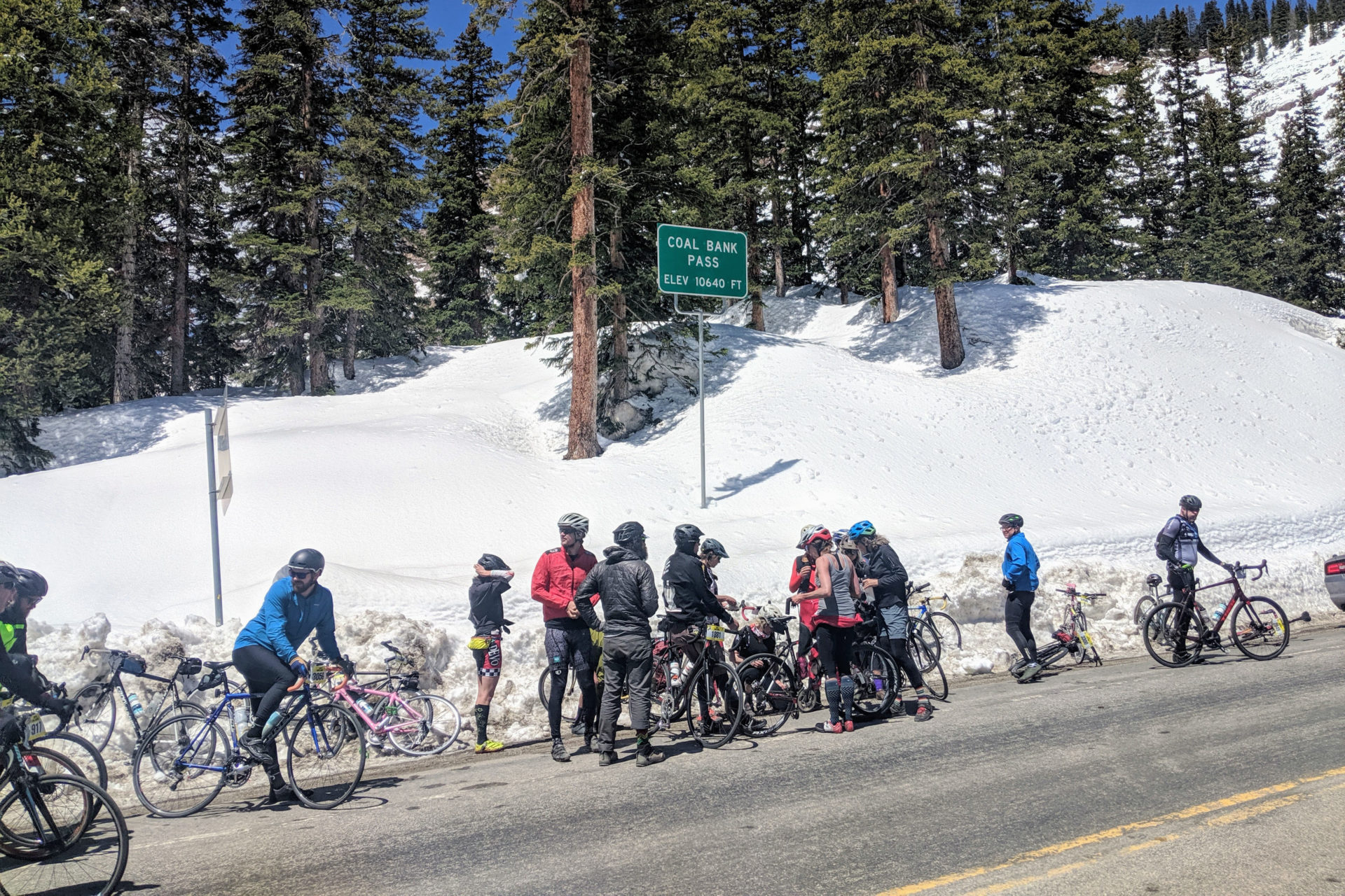 A group of people standing with their bikes on the edge of a mountain road. There is a road sign that reads "Coal Bank Pass, Elev. 10640 Ft."