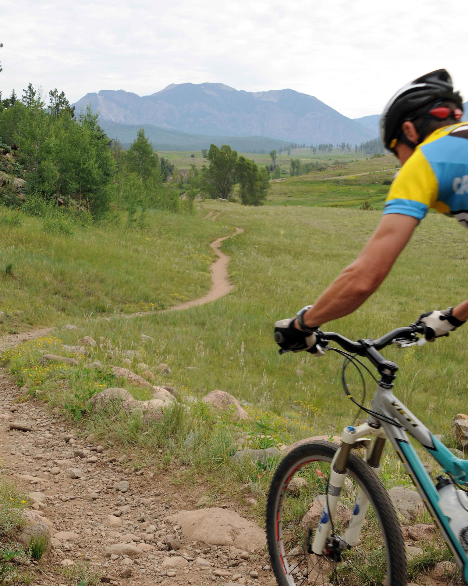 A person rides their bike on a mountain trail, with a mountain in the background.
