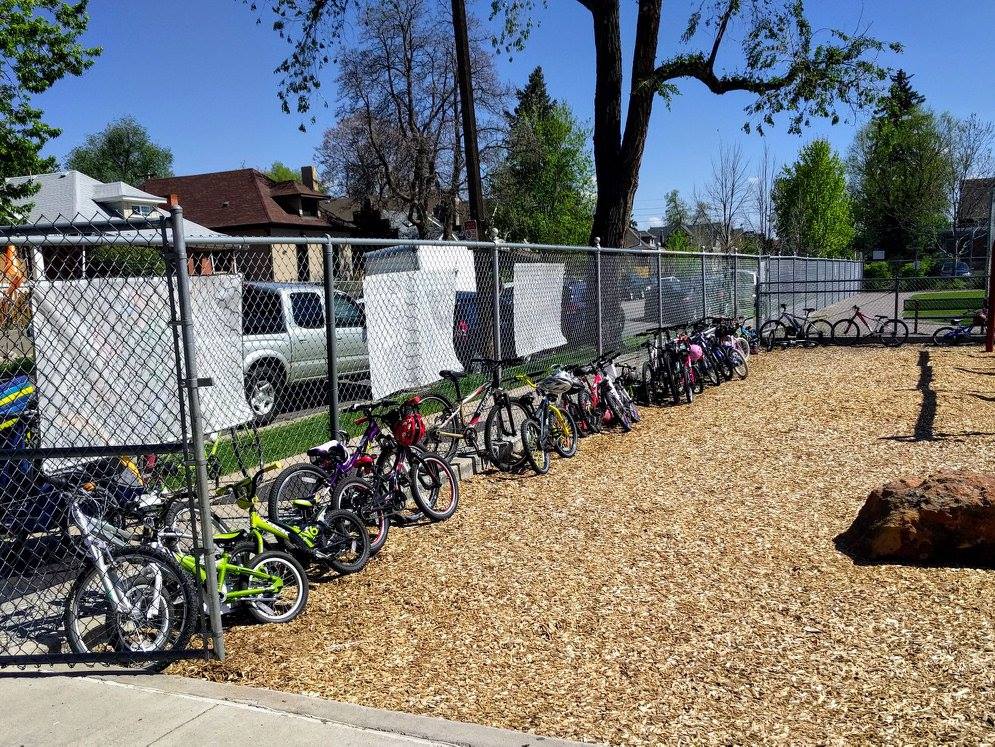 Bike racks by the school that are filled with children's bikes. There is a fence behind them.