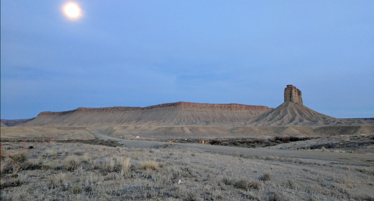 A cliff and a vertical rock formation at dusk.