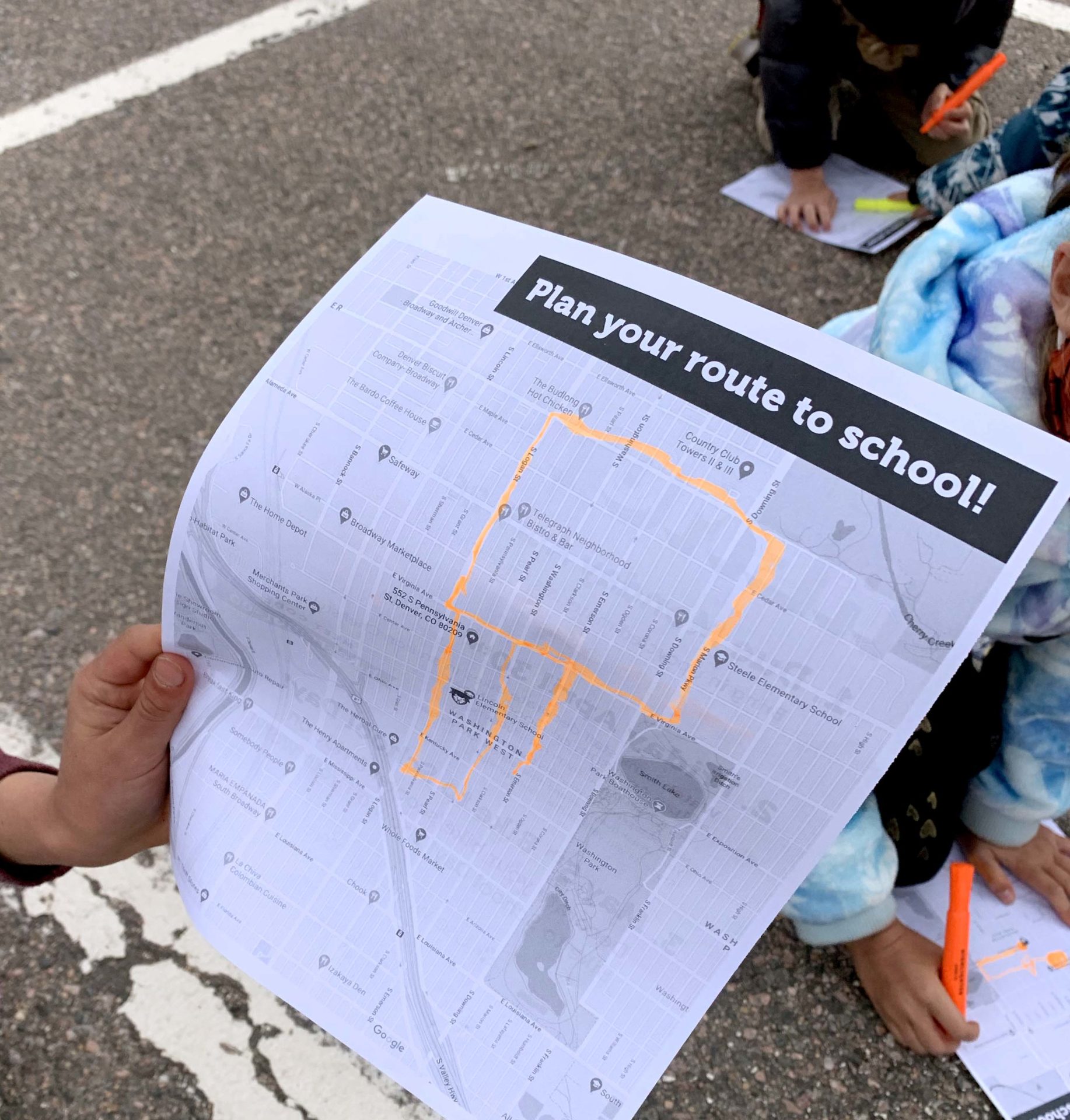 A hand holding a piece of paper that features a map with a route highlighted, and says "Plan your route to school!"
