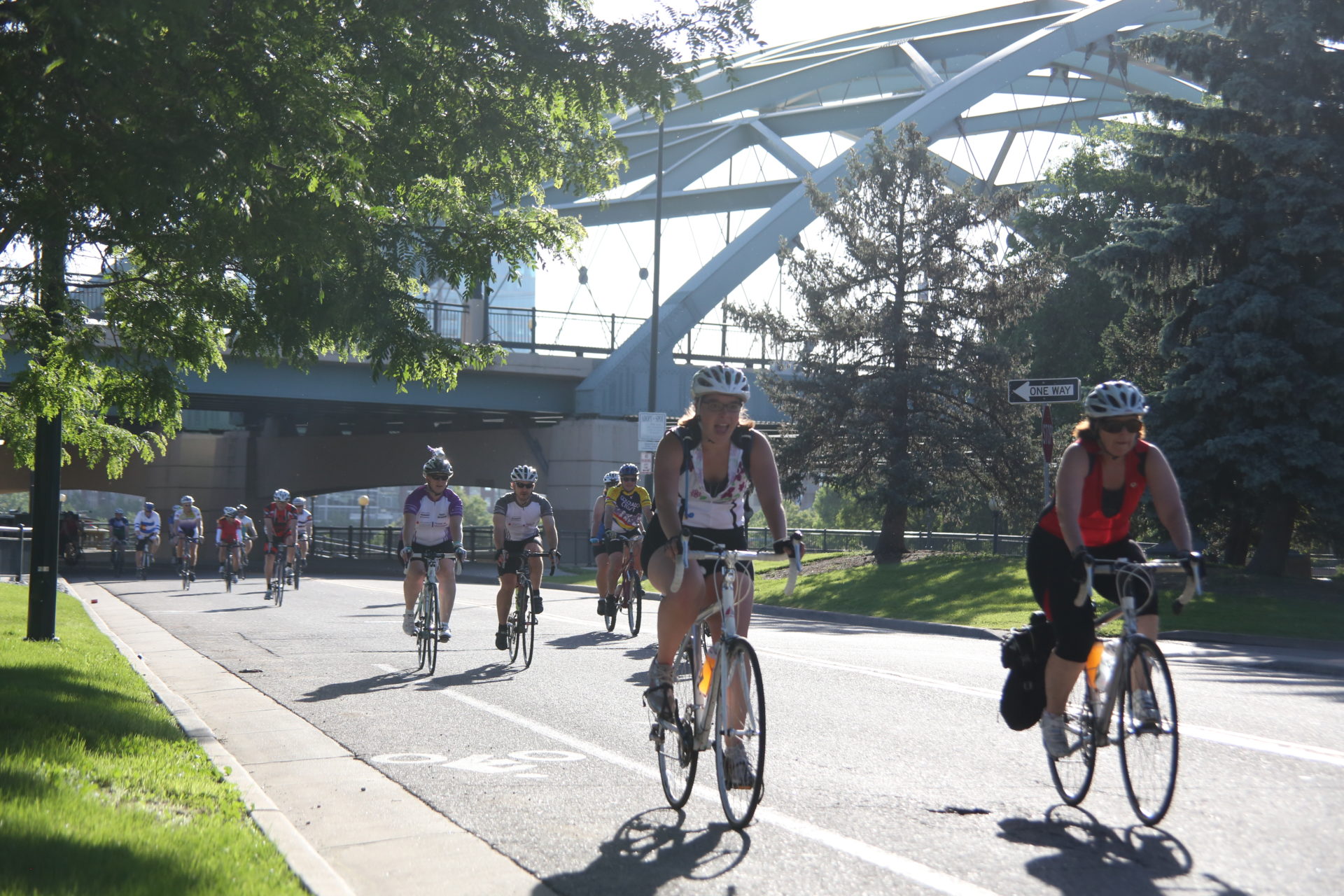 dcr downtown bridge A group of people ride bikes on a paved road to the foreground right of the frame. In the background, there is a bridge under which the riders are biking.