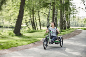 A person rides a handcycle trike on a paved trail.