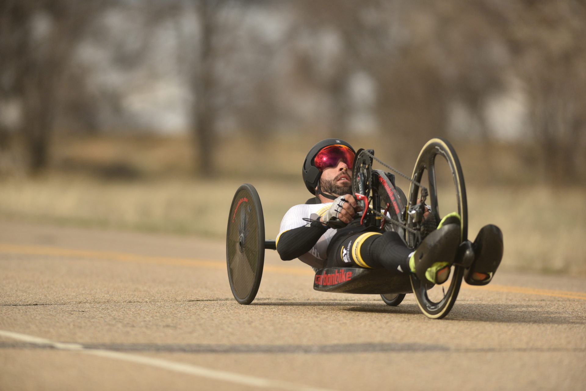 A person riding a flat recumbent trike on a paved road toward the bottom right of the frame.