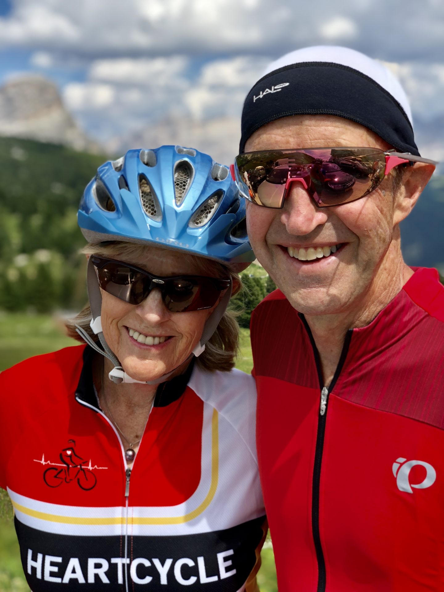 A white man and woman wearing bike jerseys and helmets smile. They are photographed from chest up.