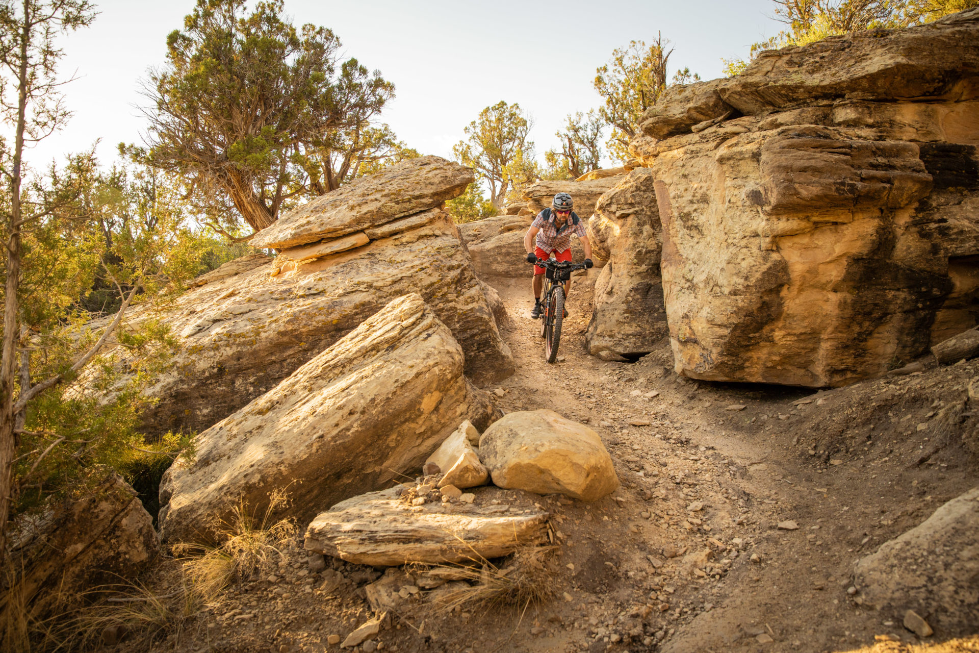 A person rides a mountain bike down a trail flanked by large rocks.