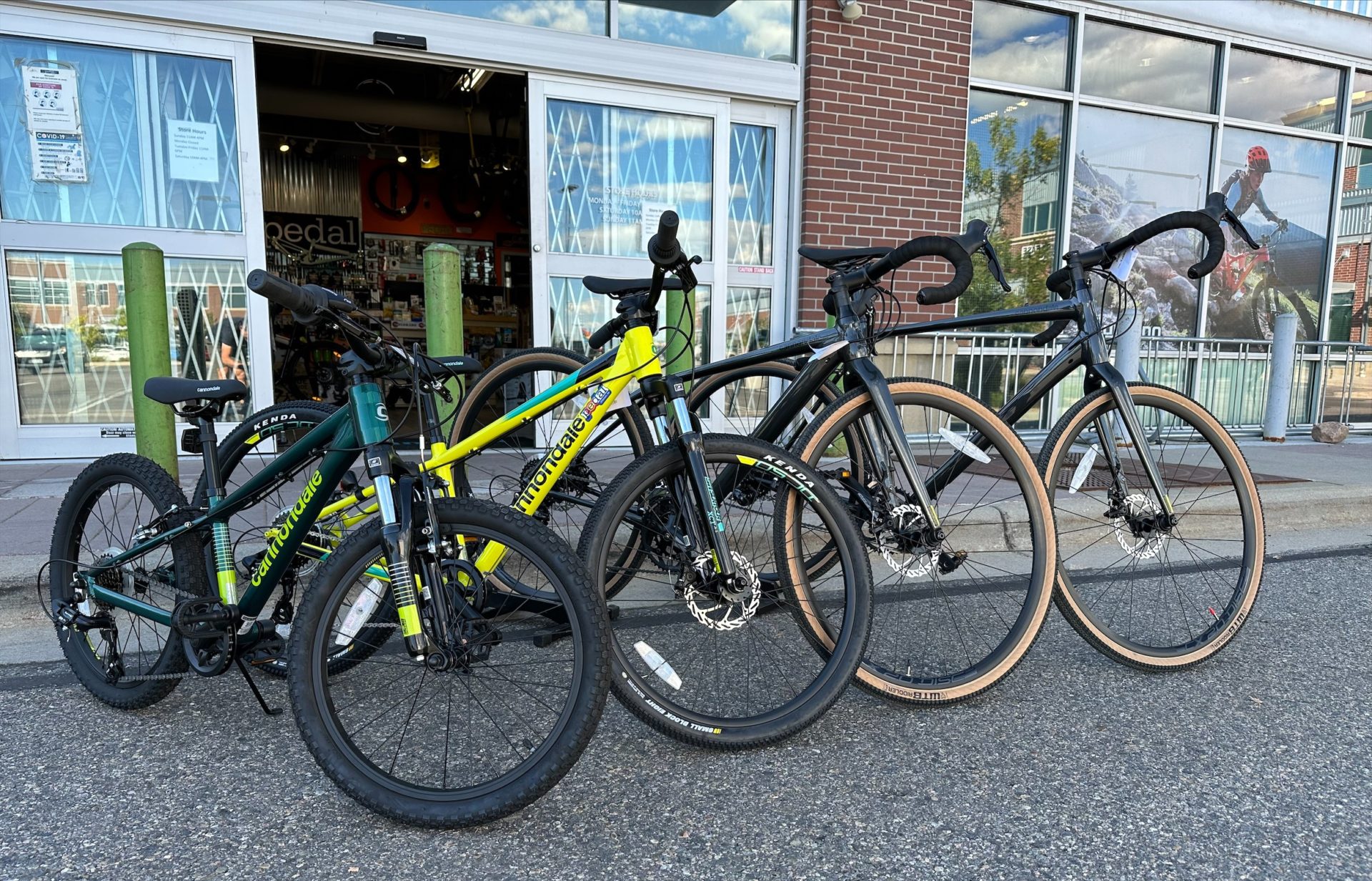 Four bikes parked in front of the Pedal of Littleton bike shop; 2 adults and 2 kids.