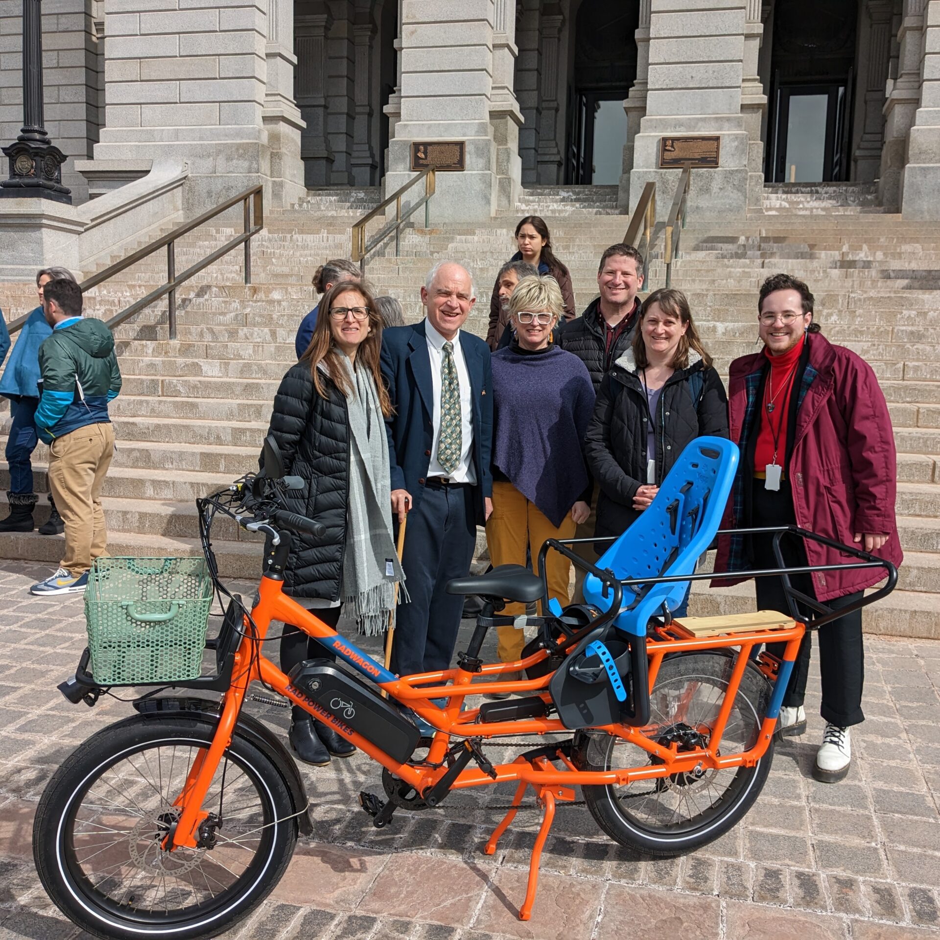 A group of people stand in front of the steps of the Colorado State Capitol with an eCargo bike.