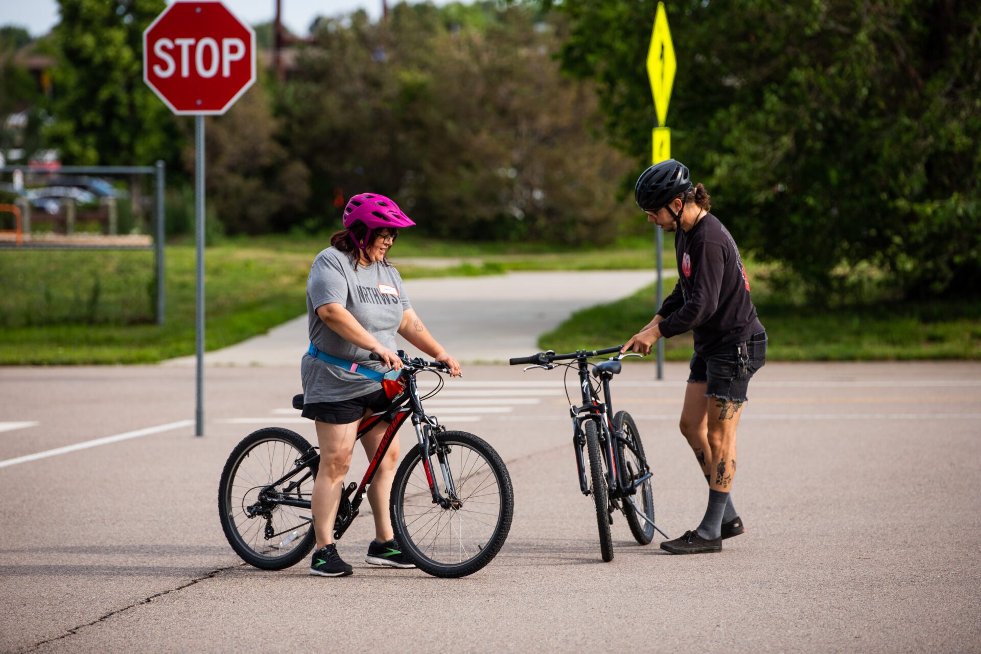 A person standing over a bike speaking with another person standing and holding up a bike.