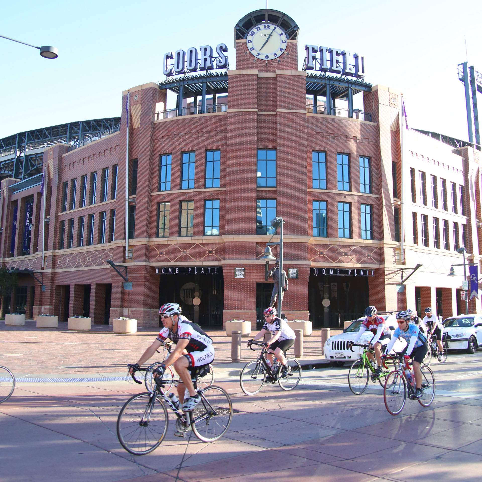 a group of people on bikes rides in front of Coors Field