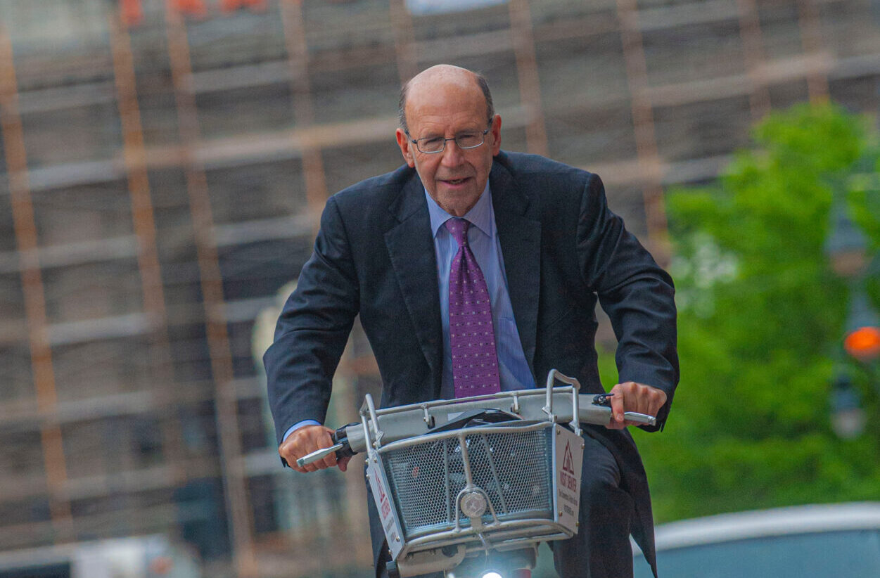 Steve Sander, wearing a suit and tie, riding a red Denver B-Cycle near Denver Union Station