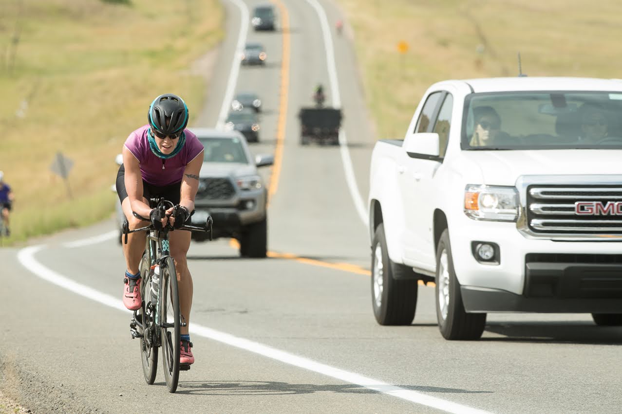 Bike rider riding on shoulder of road with cars in the background